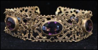 A 1920s gold-tone filigree work 5 link panel bracelet set with faceted amethyst glass. Measures