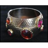 A 1960's gold tone oversized bangle set with large faceted pink and orange stones with planished