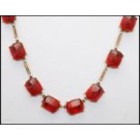 A 1920s German gold-tone red scarab glass cabochon riviere necklace having stylised cabochons.