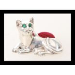 A silver pincushion in the form of a cat having green stone eyes and a red cushion to its back.