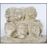 A clay sculpture depicting 14 grotesque male heads displaying different moods protruding from a