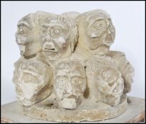 A clay sculpture depicting 14 grotesque male heads displaying different moods protruding from a