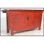 A Chinese 19th / 20th century large red lacquer sideboard of shaped form. The worn flared top over