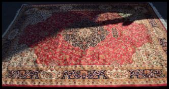 A Persian Islamic Keshan carpet having a red ground with floral patterning and a blue border.