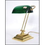 A vintage 20th century bankers desk lamp having an adjustable green glass shade raised on a brass