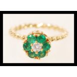 An 18ct gold twist flower head ring set with six brilliant cut emeralds around a central diamond.