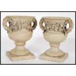 A pair of antique style white marble type composite urns raised on square bases with grape and