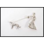 A silver Art Deco style brooch of a lady walking her dog attached by a chain having marcasite accent