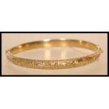 A hallmarked 9ct gold bangle with a hinged opening and safety chain with floral engraving.