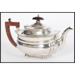 An early 20th century silver hallmarked teapot raised on bun feet with shaped wooden handle.