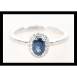 A stamped 18k white gold ring set with an oval cut central sapphire having a halo of diamonds.