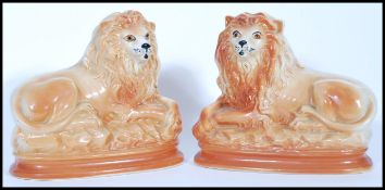 A pair of recumbent Staffordshire ceramic fire dogs in the form of lions having glass eyes and