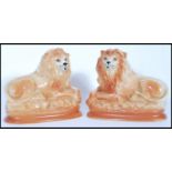 A pair of recumbent Staffordshire ceramic fire dogs in the form of lions having glass eyes and