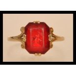 An early 20th century hallmarked 9ct gold ring set with an octagon cut red stone and scrolled