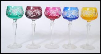 A group of five early 20th century coloured glass wine glasses raised on faceted circular foot