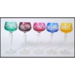 A group of five early 20th century coloured glass wine glasses raised on faceted circular foot