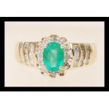 A stamped 14ct gold ring set with a central oval cut emerald and diamond accent stones to the head