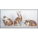 A group of three royal crown derby china cat paperweights to include two one Imari style paperweight