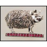 A stamped sterling silver brooch in the form of a pig with engraved folate decoration, set with