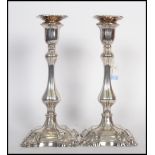 A pair of silver candlesticks raised on stepped square bases with scrolls with bulbous stem and