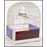 A vintage 20th Century bird cage having white bars and a wooden perch to the interior with blue