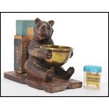 A mid 20th Century carved pine black forrest match striker in the form of a bear holding a brass