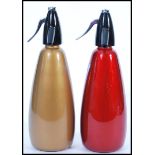 Two retro  20th century soda siphons having red and gold bodies with black and chrome tops.