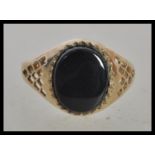 A hallmarked 9ct gold signet ring set with an oval black stone and pierced decoration to the