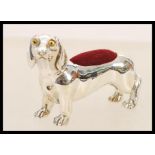 A silver pincushion in the form of a daschund dog having yellow and black glass eyes and a red