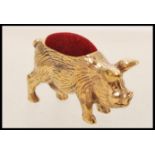 A copper pincushion in the form of a pig with engraved detailing having a red fabric cushion to
