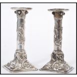 A pair of Chinese silver white metal candlesticks raised on square bases with cylindrical columns