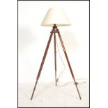 A contemporary tripod standard lamp being raised on a mahogany folding stand complete with the shade