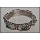 A decorative large silver bracelet with 6 individual bars adorned with cabochon green stones to
