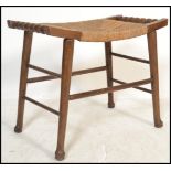 An early 20th century Arts and Crafts style squat stool raised on tapering wooden legs with rattan