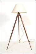 A contemporary tripod standard lamp being raised on a mahogany folding stand complete with the shade