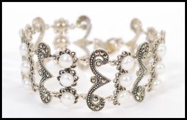 A stamped 925 silver bracelet with scrolled spacers set with marcasites and pearls. Weight 29.1g.
