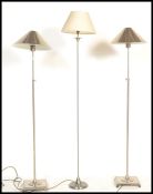 A pair of stainless steel contemporary standard lamps, each raised on squared terraced bases with