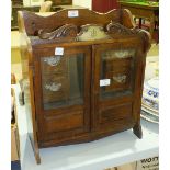 An Edwardian oak smokers' hanging wall cabinet with a pair of glazed doors, four small drawers,