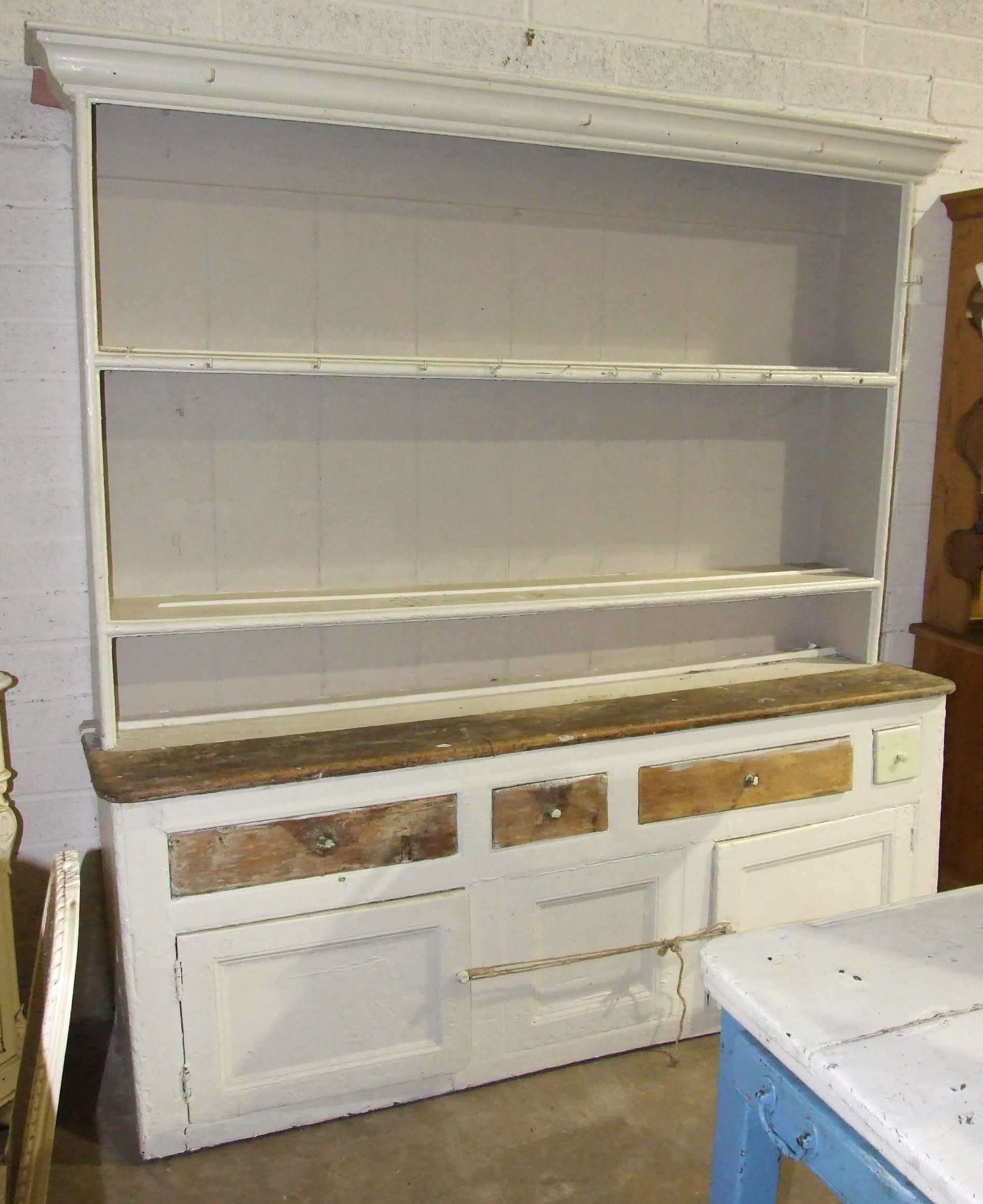 An antique rustic painted pine dresser, the moulded cornice above two shelves, the lower part fitted
