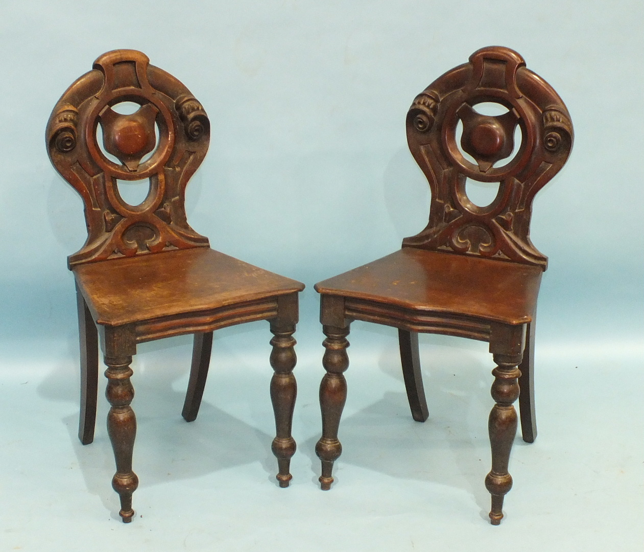 A pair of mahogany hall chairs with pierced backs and shaped solid seats, on turned front legs, (