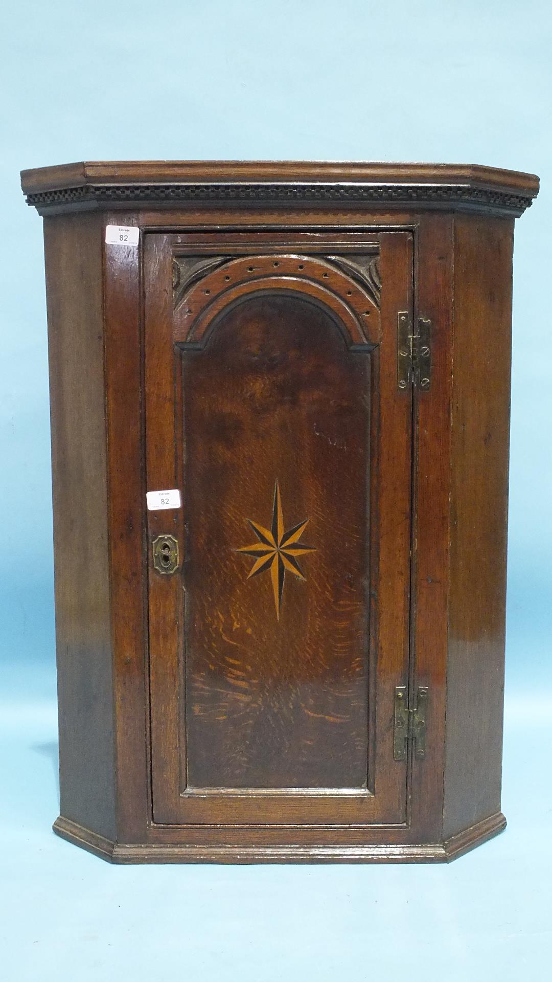 A small Georgian oak hanging corner cupboard, the panelled door with inlaid star motif, 63cm wide,