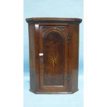 A small Georgian oak hanging corner cupboard, the panelled door with inlaid star motif, 63cm wide,