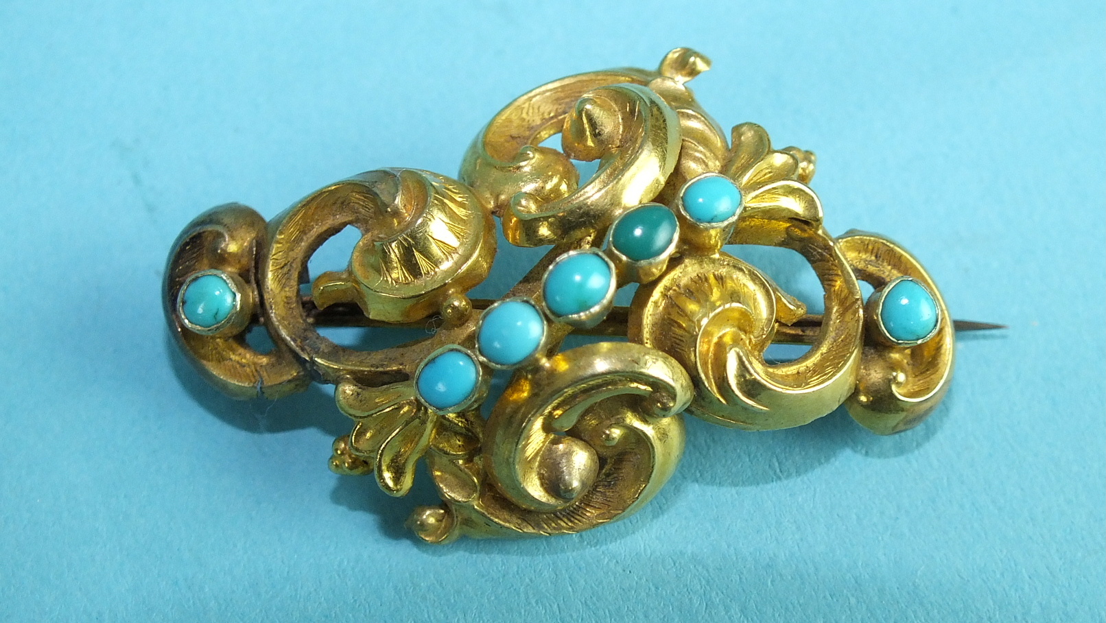 A Victorian brooch of scrolling form collet-set seven turquoises, 4.2cm, 4.8g, (repaired).