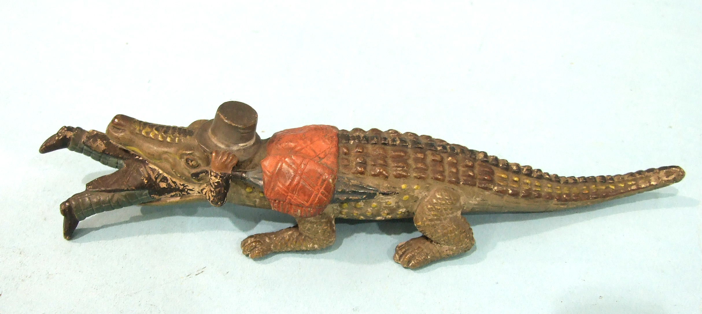A novelty composite model of a crocodile devouring a human figure carrying an umbrella and a top