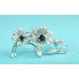 A sapphire and diamond spray brooch of two flowers with round-cut sapphire centres, within diamond-