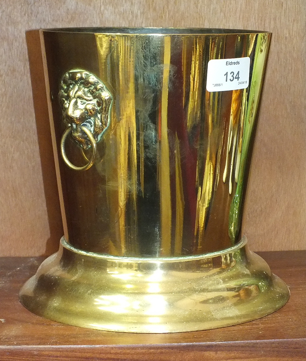 A brass wine cooler of tapering form having applied lion mask and ring handles, 17cm diameter, 19.