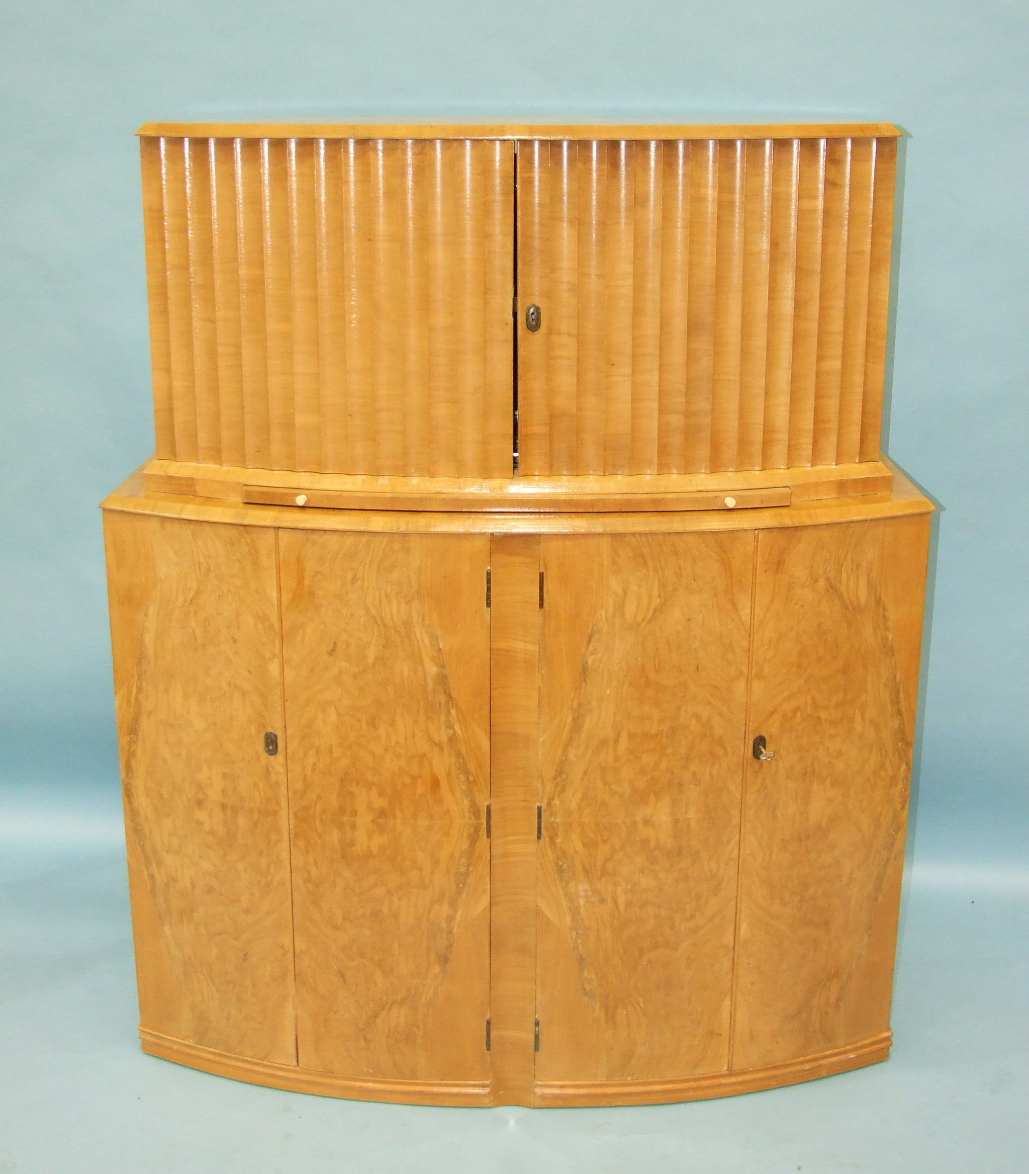 An Art Deco satin birch cocktail cabinet, having a pair of fluted hinged doors enclosing mirrored