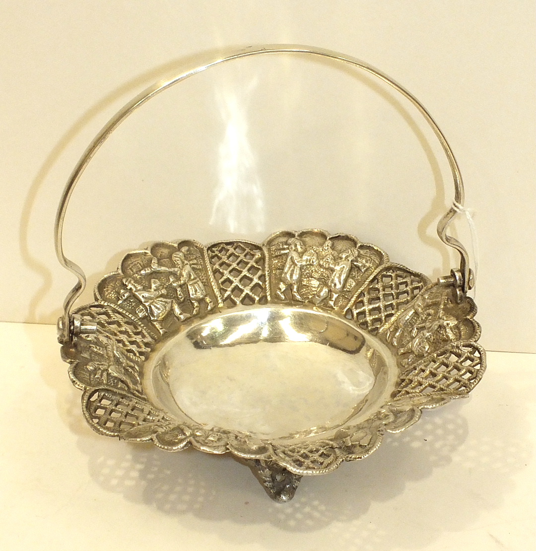 A West Asian white metal basket with swing handle decorated with embossed panels of figures