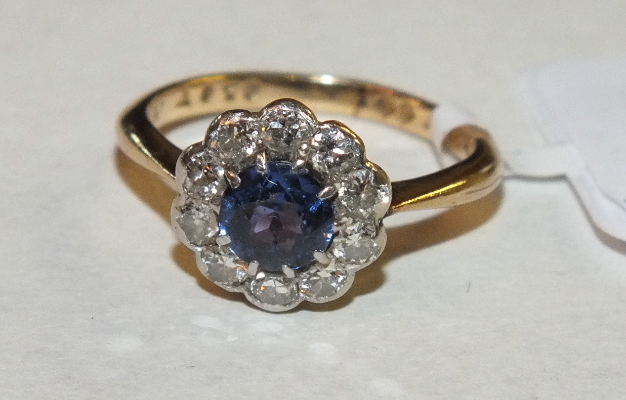 A sapphire and diamond cluster ring set round-cut sapphire of pale blue within a surround of ten