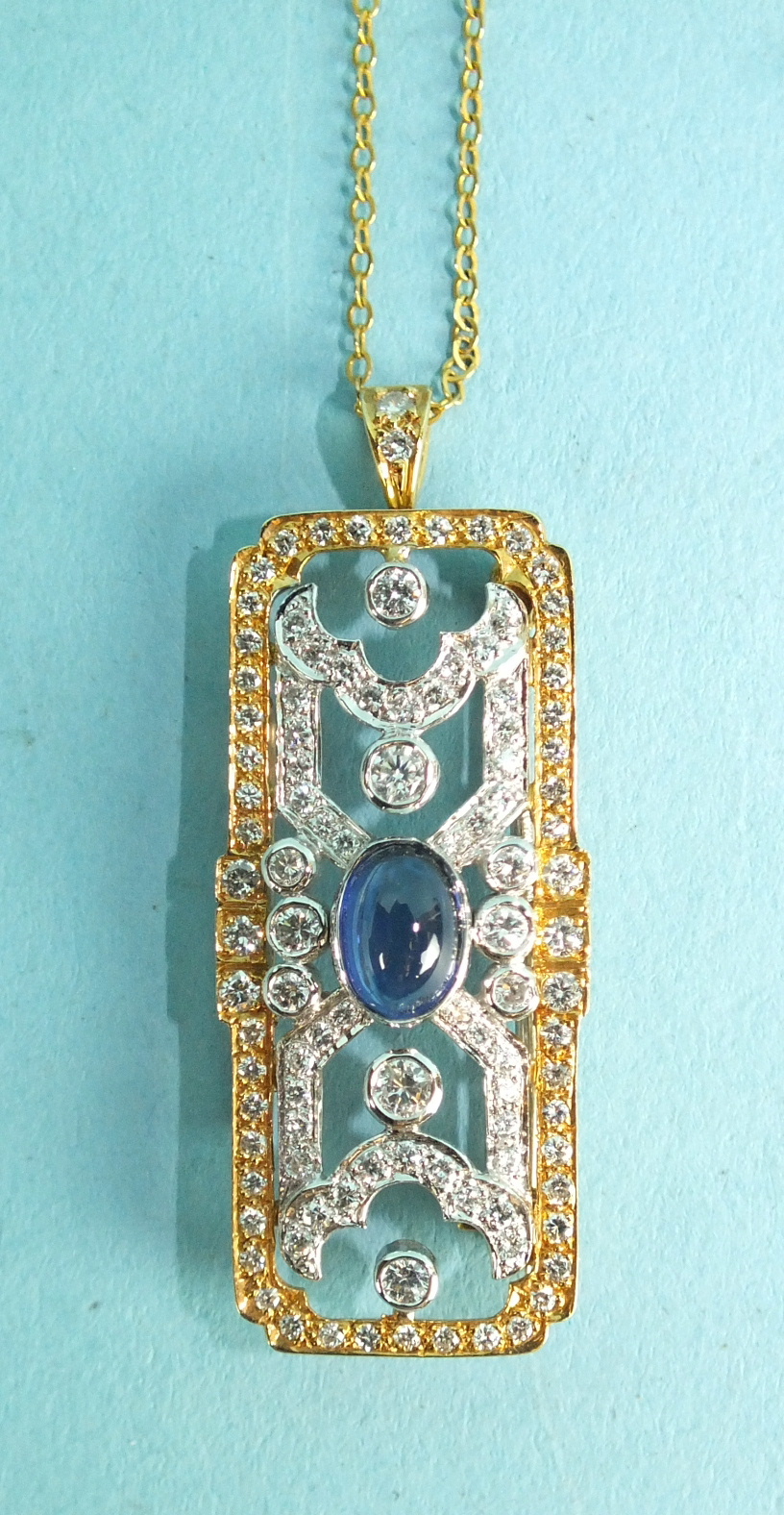 An Art-Deco-style sapphire and diamond brooch pendant centrally-set a cabochon sapphire in a